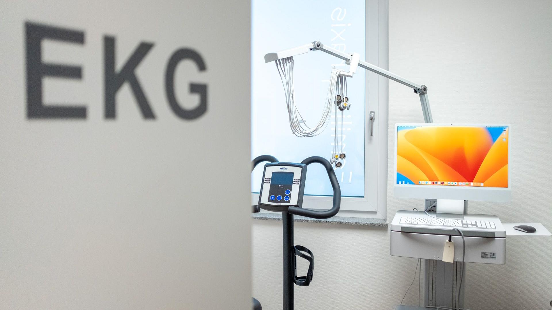 Blick ins EKG-Zimmer mit Türbeschriftung, Ergometer und EKG-Gerät.
